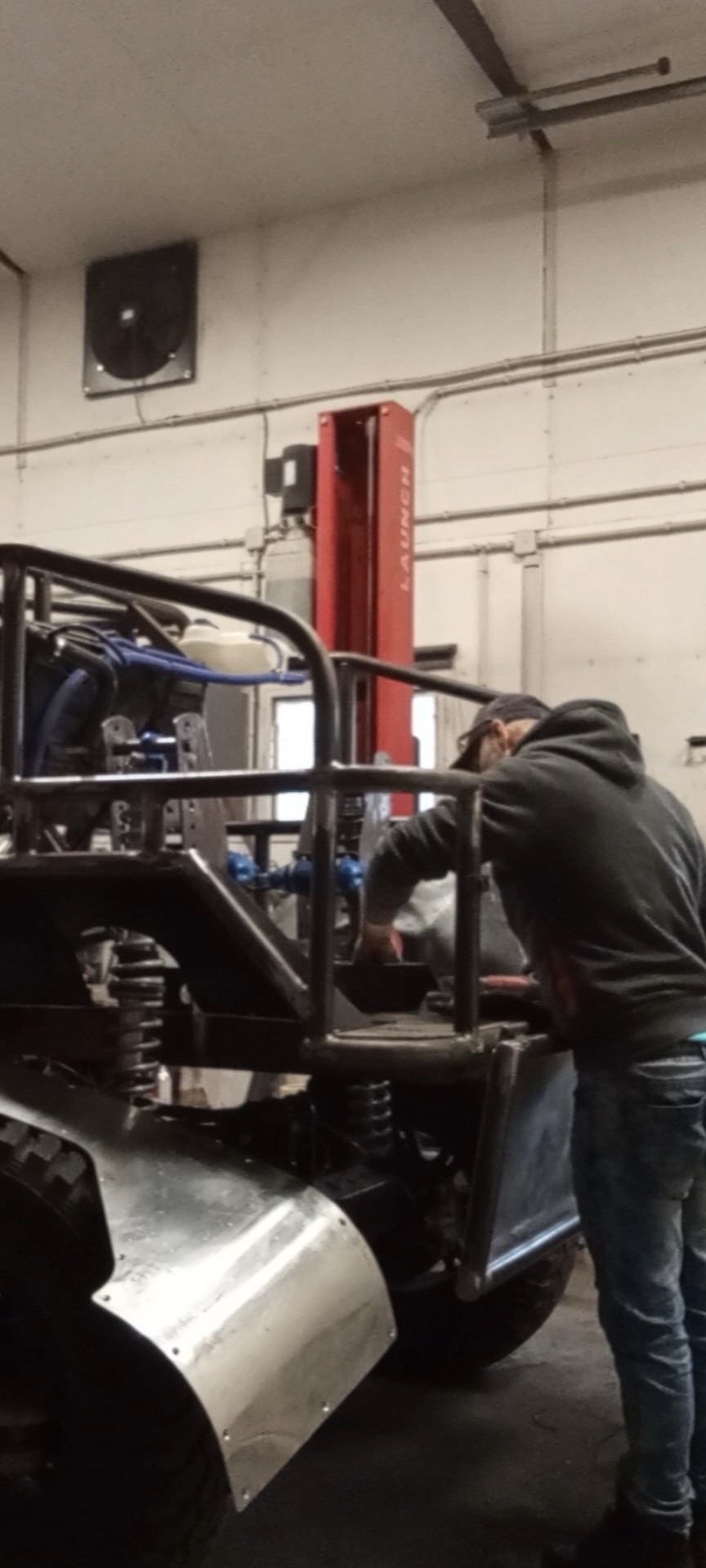 Pracownik w warsztacie podczas montażu metalowej konstrukcji pojazdu terenowego; widoczne elementy zawieszenia i karoserii.