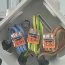 Połączenia elektryczne w puszce instalacyjnej z użyciem złączek WAGO, widok z góry. Kable w kolorach niebieskim, zielono-żółtym i brązowym.