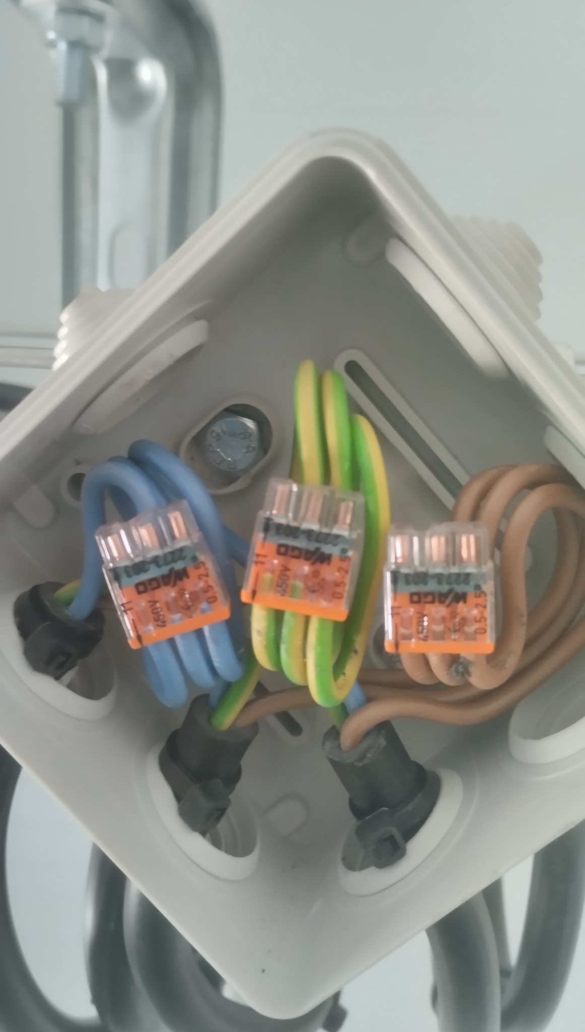 Połączenia elektryczne w puszce instalacyjnej z użyciem złączek WAGO, widok z góry. Kable w kolorach niebieskim, zielono-żółtym i brązowym.