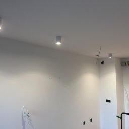 eFLOW - Nowoczesne, białe lampy sufitowe typu downlight, równomiernie rozmieszczone w jasnym pomieszczeniu. Widoczne kable i puszki instalacyjne, sugerujące etap wykończeniowy.