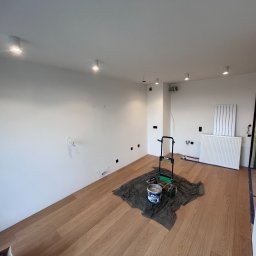 eFLOW - Wnętrze pokoju po montażu oświetlenia punktowego, widoczne przygotowania do malowania ścian, podłoga drewniana, grzejnik na ścianie.