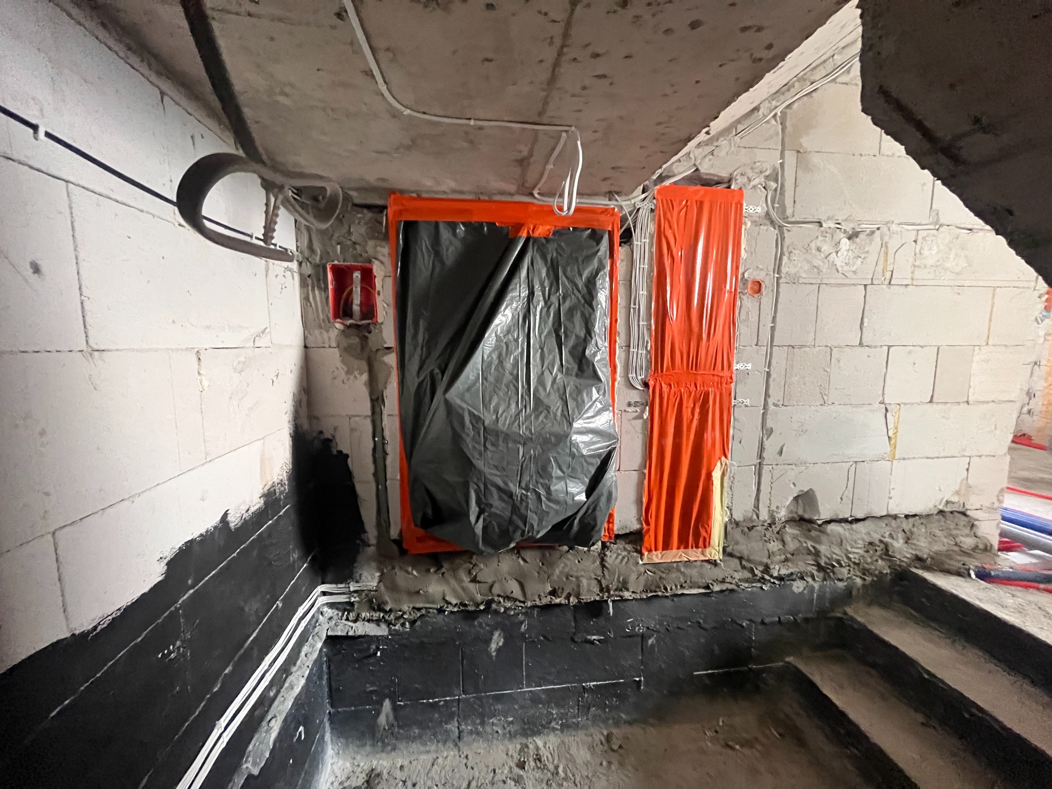 Instalacja elektryczna w surowym wnętrzu: kable prowadzone wzdłuż ścian z betonu komórkowego, zabezpieczone folią okna i puszki. Widoczne przewody pod sufitem.