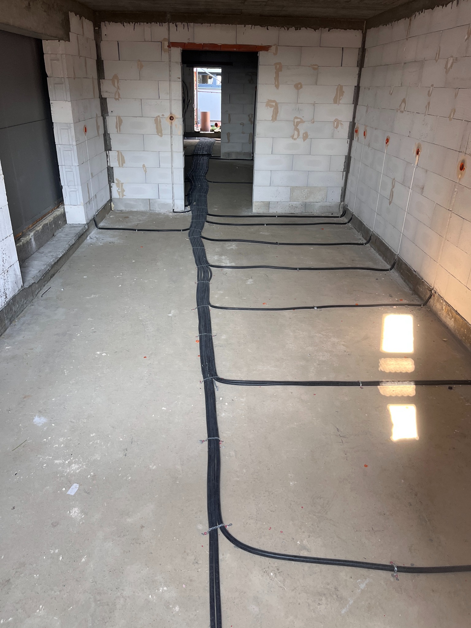 Surowy stan: instalacja elektryczna w peszlu na podłodze, ściany z betonu komórkowego z puszkami. Widok z góry, brak wykończenia.