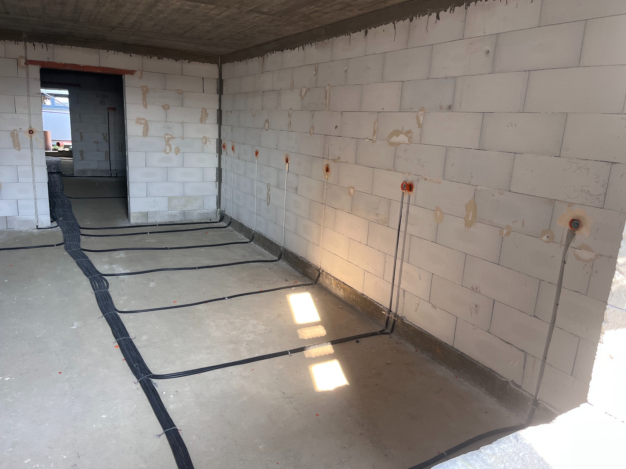 Surowy stan: przewody elektryczne ułożone wzdłuż ścian i podłogi, z puszkami w ścianach z betonu komórkowego, przygotowane do dalszych prac wykończeniowych.