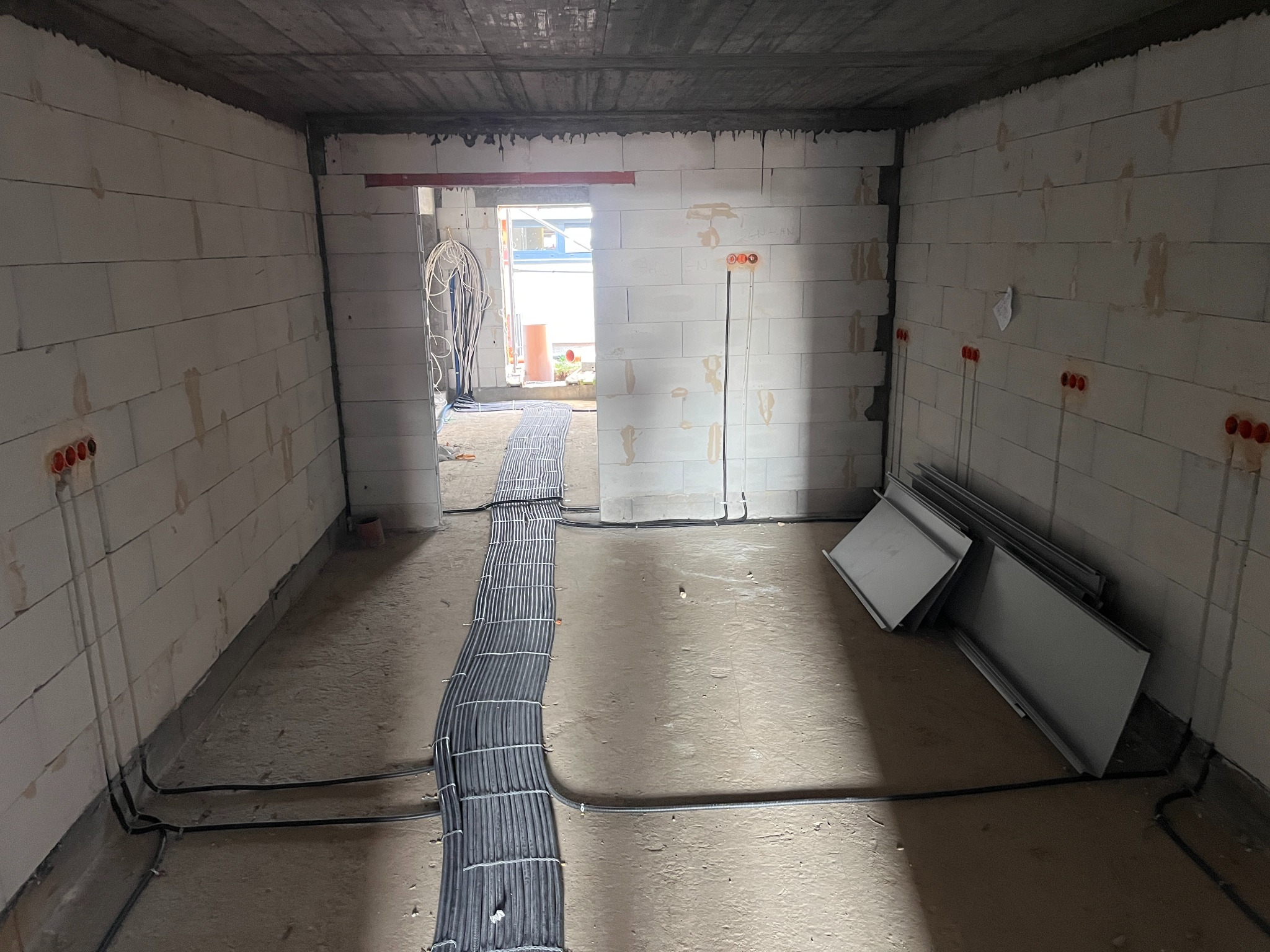 Wnętrze w trakcie prac elektrycznych: kable w podłodze, puszki instalacyjne w ścianach z betonu komórkowego. Widoczne płyty do montażu. Surowy stan.