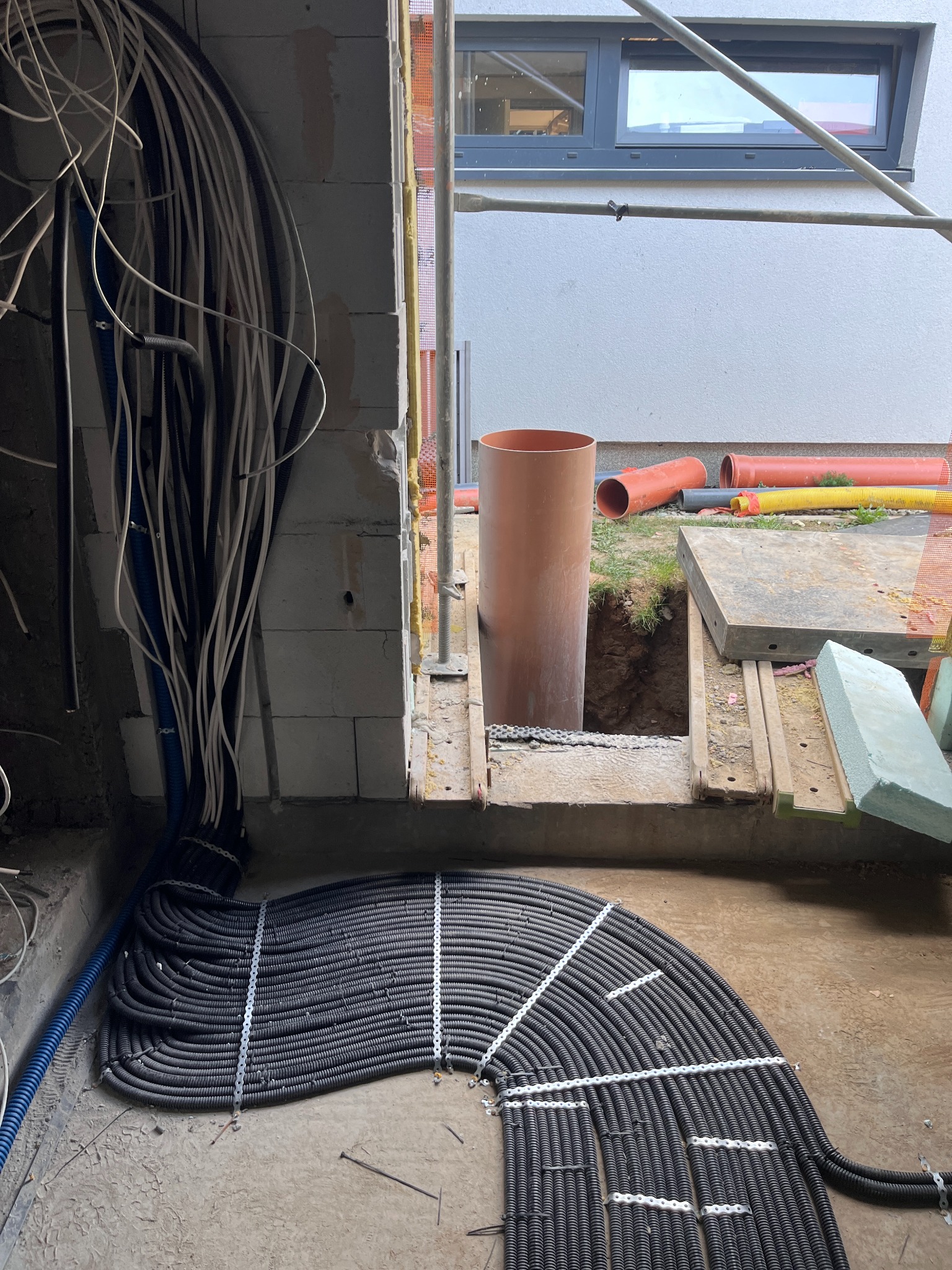 Układanie peszli i kabli w nowym budynku w trakcie budowy. Widoczne przewody, rury i elementy konstrukcyjne. Etap prac instalacyjnych przed zalaniem posadzki.