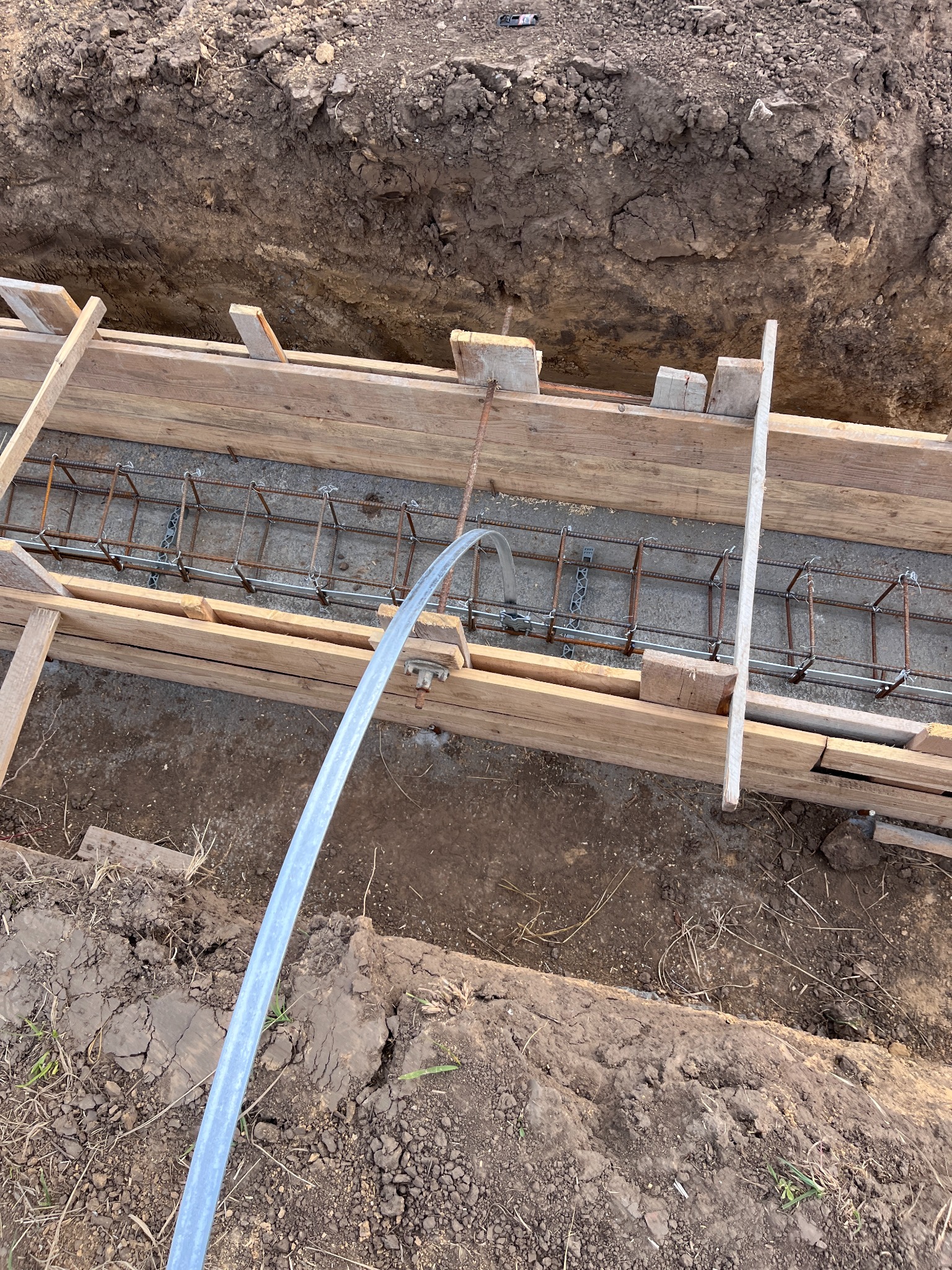 Ziemny wykop z drewnianym szalunkiem i zbrojeniem, przygotowany do wylania fundamentów. Widoczny peszel elektryczny. Ujęcie z góry.