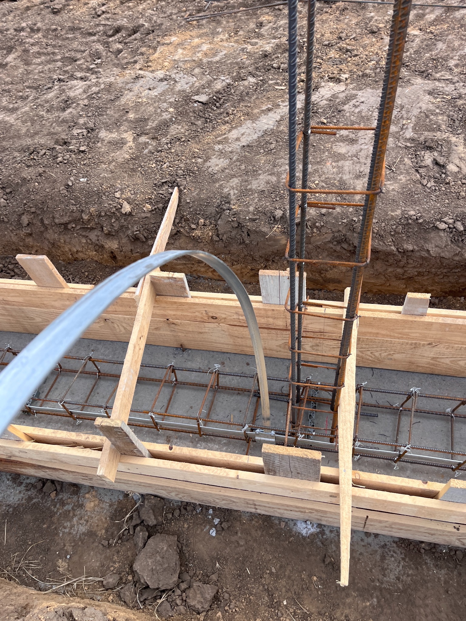 Zbrojenie fundamentów w drewnianym szalunku, widok z góry. Stalowe pręty zbrojeniowe połączone drutem, przygotowane do zalania betonem. Grunt wokół wykopu.
