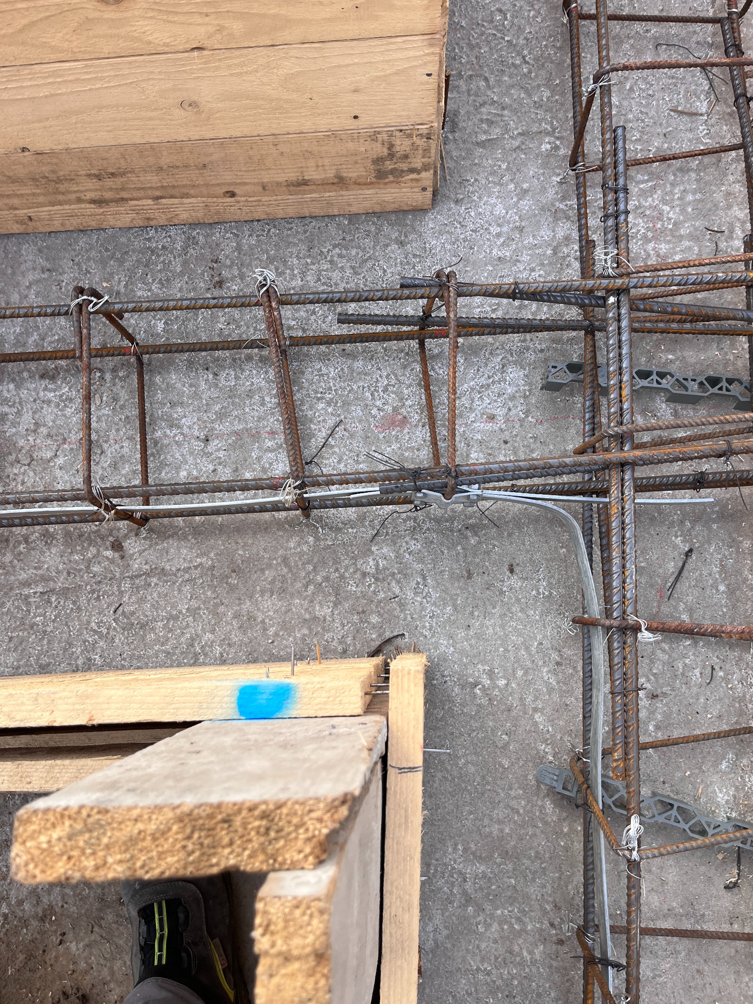 Zbrojenie fundamentów z widocznymi elementami konstrukcyjnymi i przewodami elektrycznymi. Kąt ujęcia z góry, betonowe podłoże.