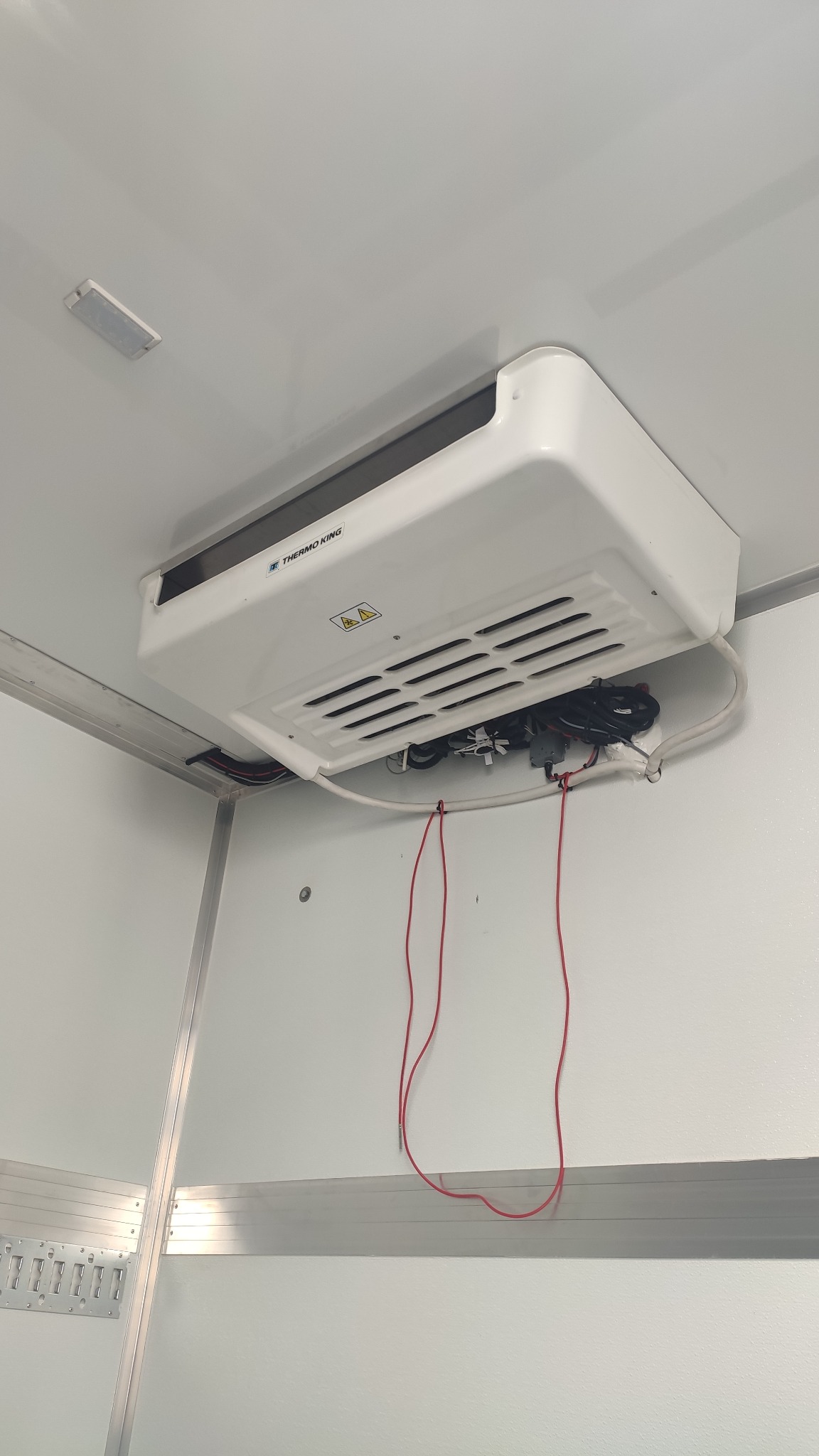 Wnętrze chłodni busa z zamontowanym agregatem Thermo King. Widoczne okablowanie, białe panele ścian i sufitu. Detal agregatu chłodniczego.
