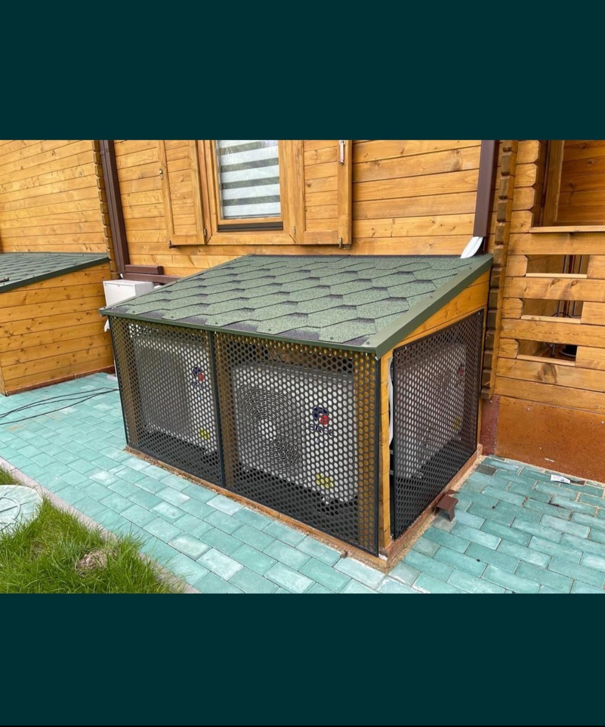 Zabudowa dwóch klimatyzatorów zewnętrznych zadaszona i zabezpieczona metalową siatką na tle drewnianego domu, na zewnątrz.