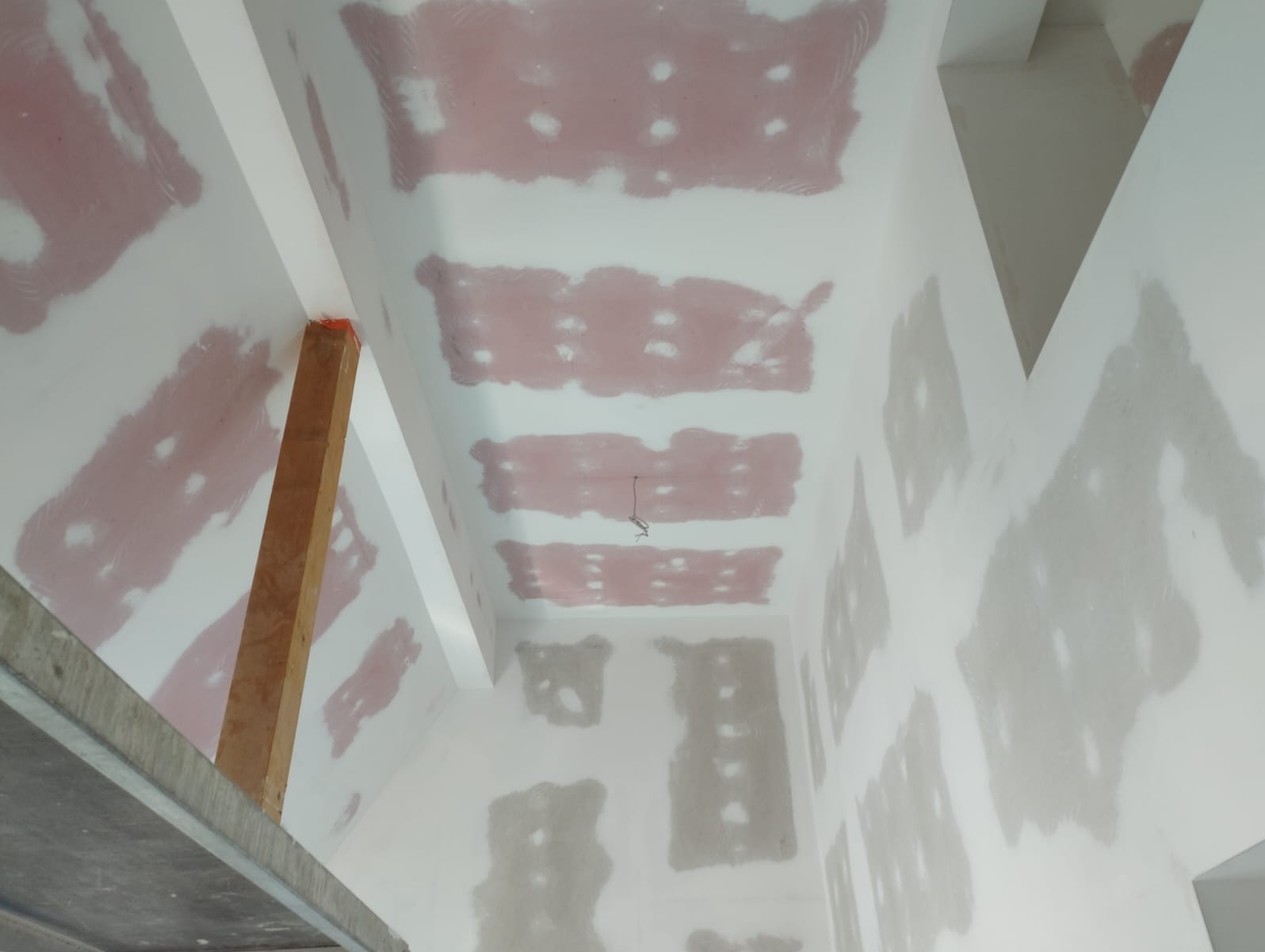 Ściana i sufit po szpachlowaniu, widoczne fragmenty różowej szpachli, przygotowane do dalszych prac wykończeniowych. Widok z dołu, fragment rusztowania.