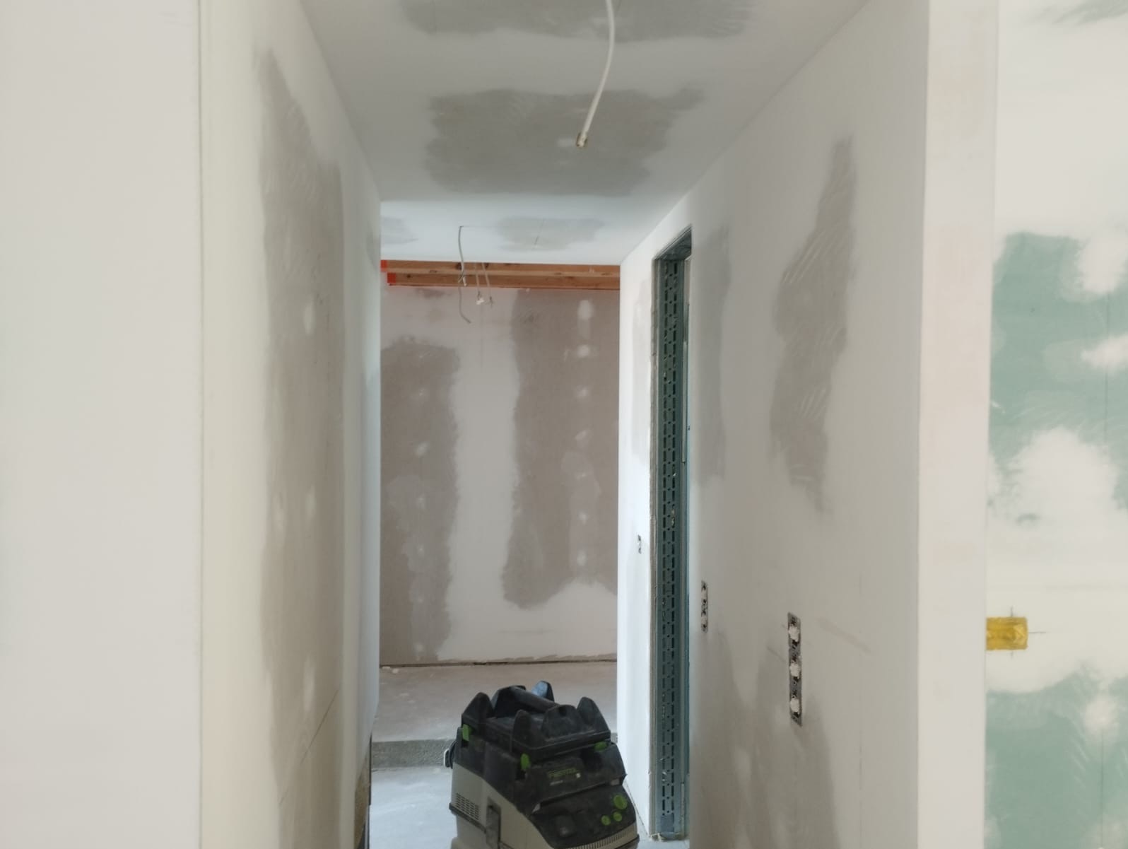 Korytarz w trakcie szpachlowania ścian, widoczne ślady gładzi i szlifierka. Surowy stan wykończenia wnętrza.
