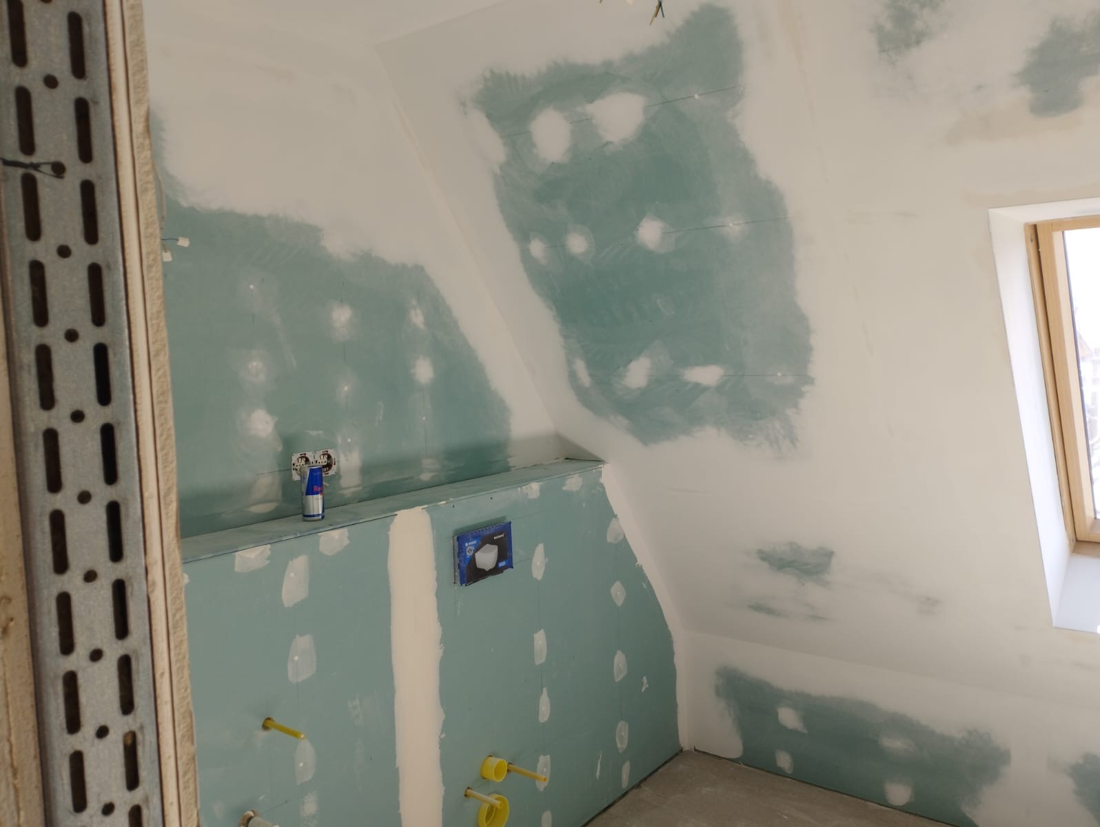 Poddasze w trakcie adaptacji: ściany i skosy obłożone płytami gipsowo-kartonowymi, widoczne łączenia szpachlowane, instalacje sanitarne przygotowane do montażu.