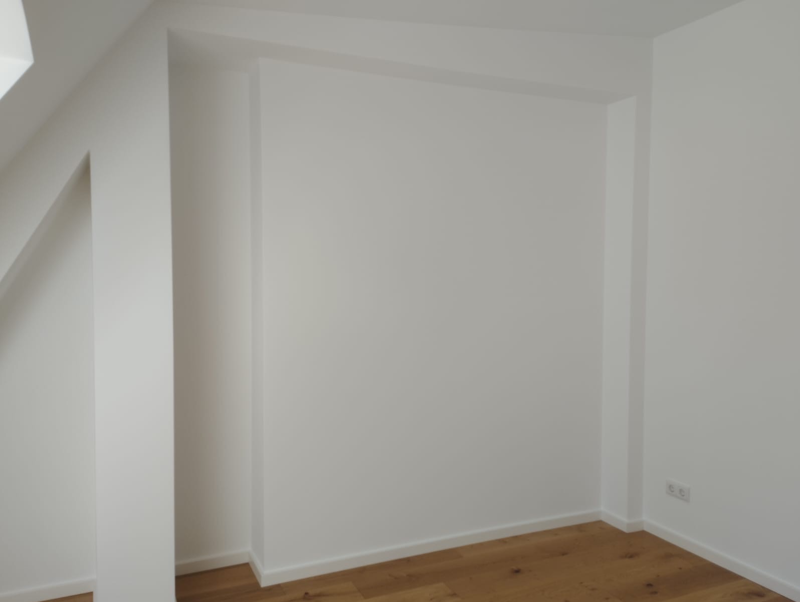Białe, świeżo pomalowane ściany w rogu pokoju z drewnianą podłogą. Widoczne gniazdka elektryczne. Minimalistyczne wykończenie wnętrza.