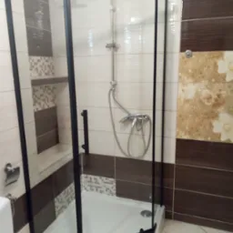 Nowoczesna kabina prysznicowa z czarnymi profilami, jasne płytki z dekorami w beżach i brązach. Widoczny zestaw prysznicowy i fragment toalety.