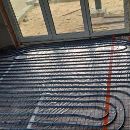 DAW-MON MONIKA WALKOWIAK - Niebieskie rury ogrzewania podłogowego ułożone na izolacji z folii aluminiowej w surowym wnętrzu, widok z góry na instalację przed wylewką.