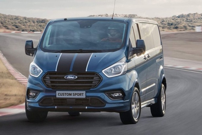 Niebieski Ford Transit Custom Sport z czarnymi pasami na masce, dynamicznie prezentowany na torze wyścigowym. Widoczne detale: logo Forda i oznaczenie modelu.