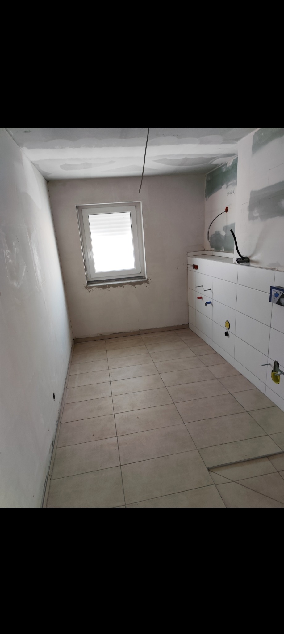 Łazienka w trakcie remontu: położone płytki podłogowe i częściowo ścienne, ściany przygotowane do malowania, widoczne instalacje wodne.