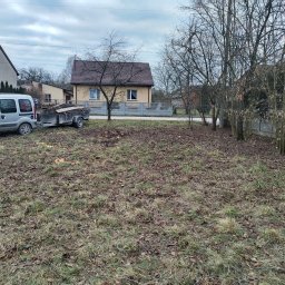 Wujo Sebastian wujek - Przygotowany teren po wycince drzew, z przyczepą pełną gałęzi i pni. W tle domy jednorodzinne i pochmurne niebo.