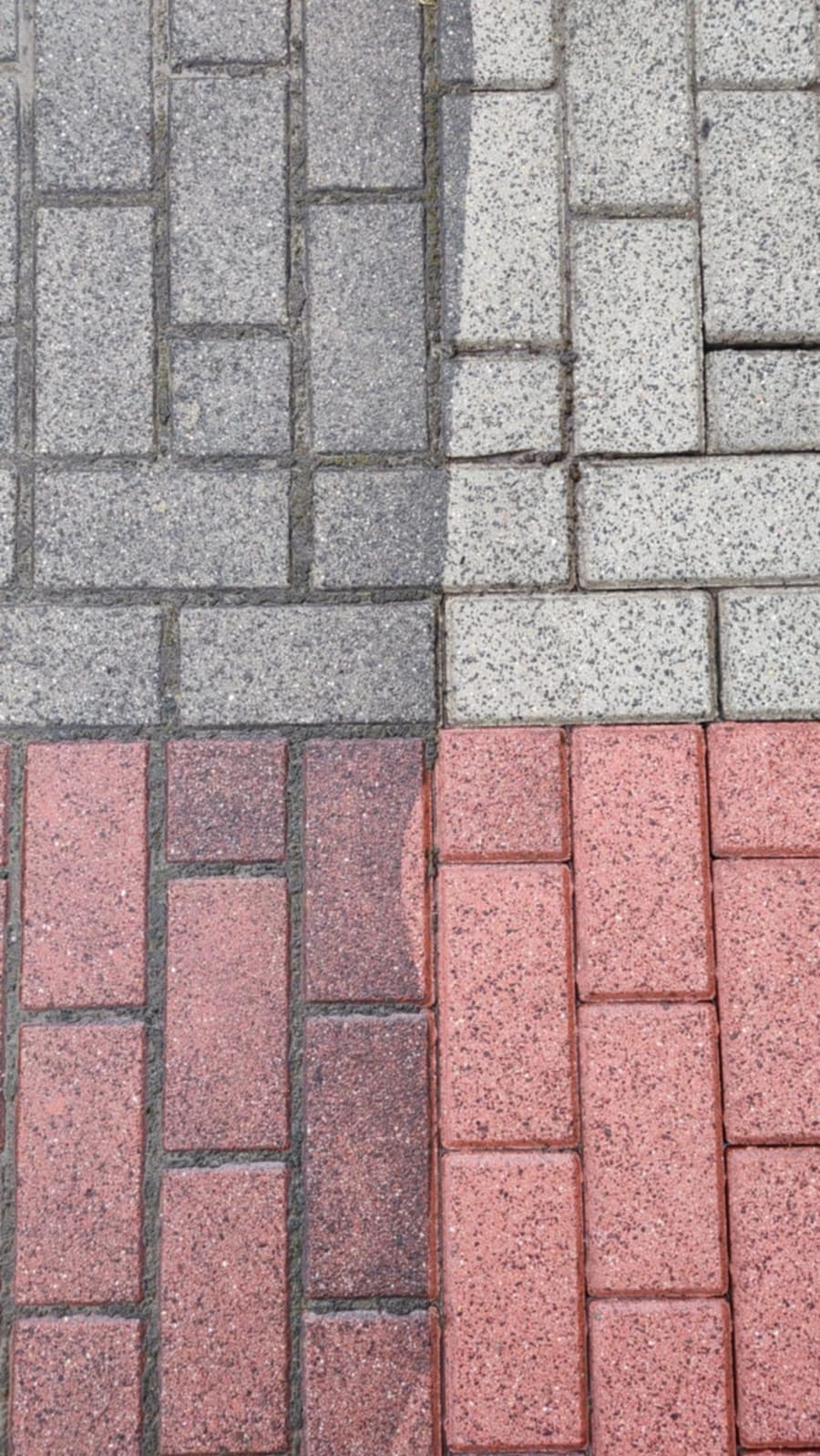 Częściowo umyta kostka brukowa w odcieniach szarości i czerwieni. Widoczna różnica w kolorze i czystości między umytą a brudną powierzchnią. Perspektywa z góry.