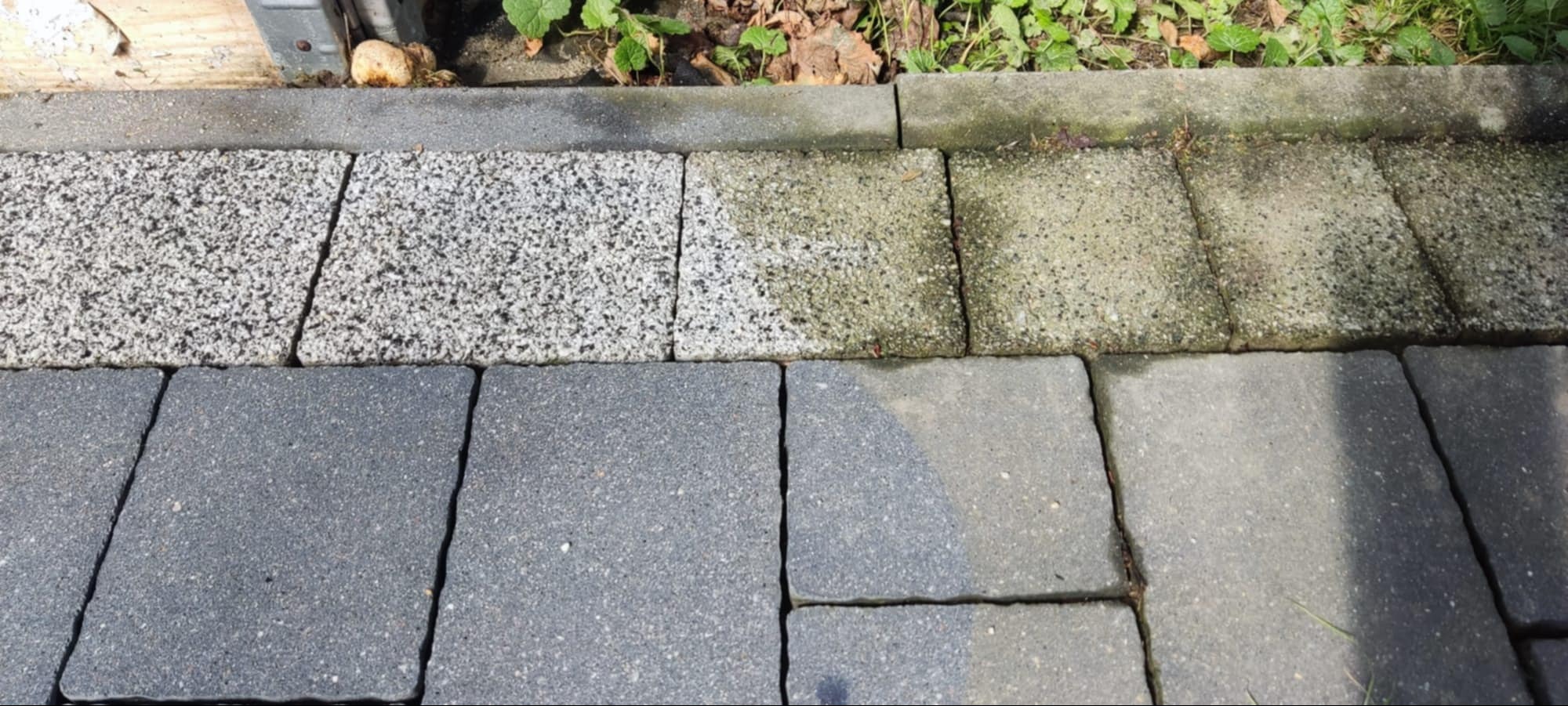 Fragment kostki brukowej po czyszczeniu, widoczna różnica między umytą a zabrudzoną powierzchnią. Górna część kostki jaśniejsza, dolna ciemniejsza.