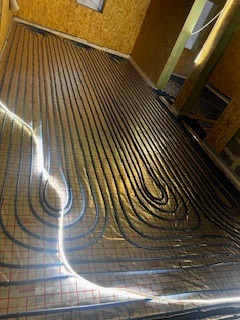 Ułożone rury ogrzewania podłogowego na folii odblaskowej, widok z góry, przed wylaniem posadzki. Czarny przewód tworzy pętle na całej powierzchni podłogi.