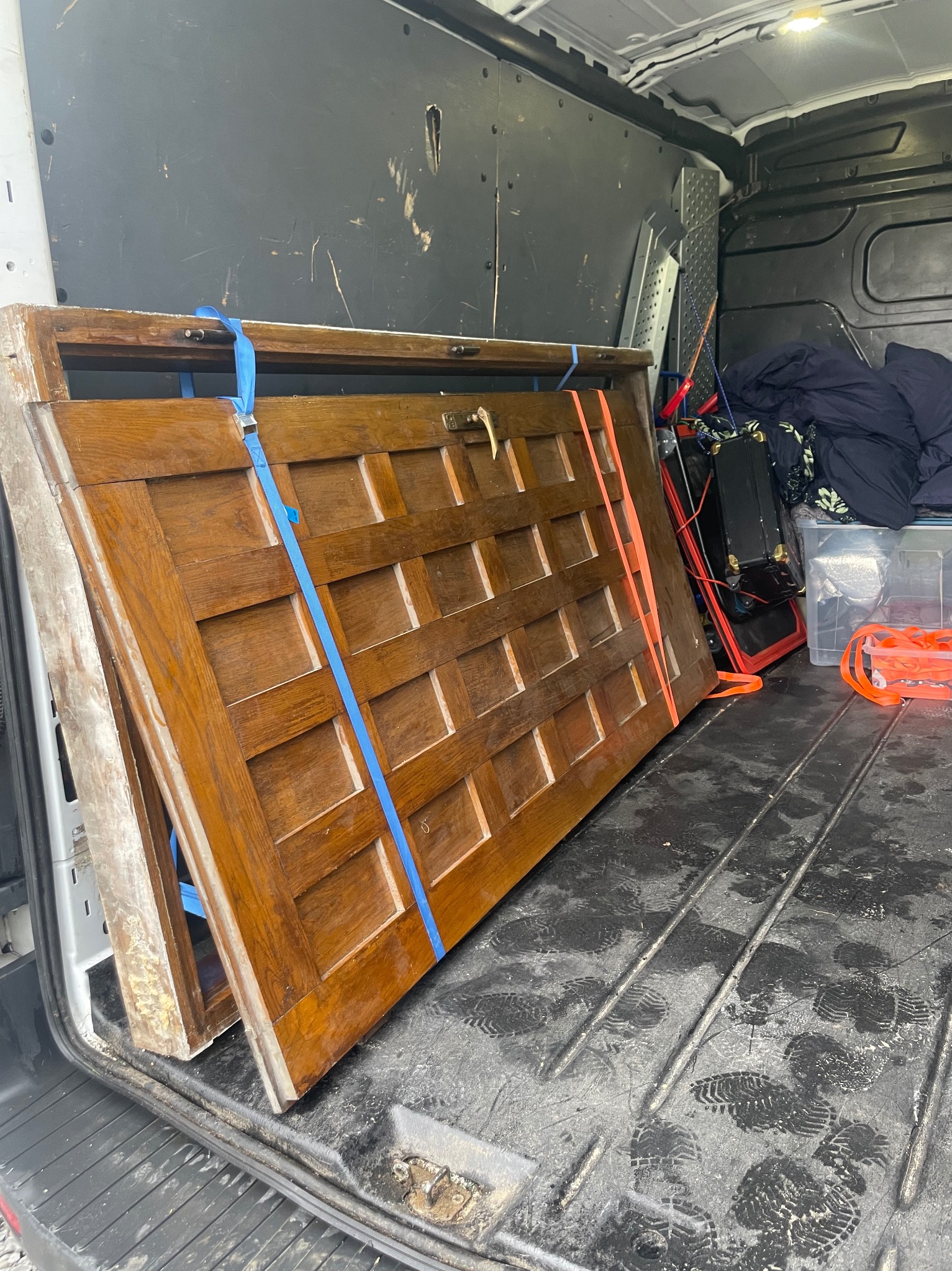 Dwie drewniane drzwi zabezpieczone pasami wewnątrz busa transportowego w Tczewie. Widoczne ślady użytkowania na podłodze i ścianach pojazdu.