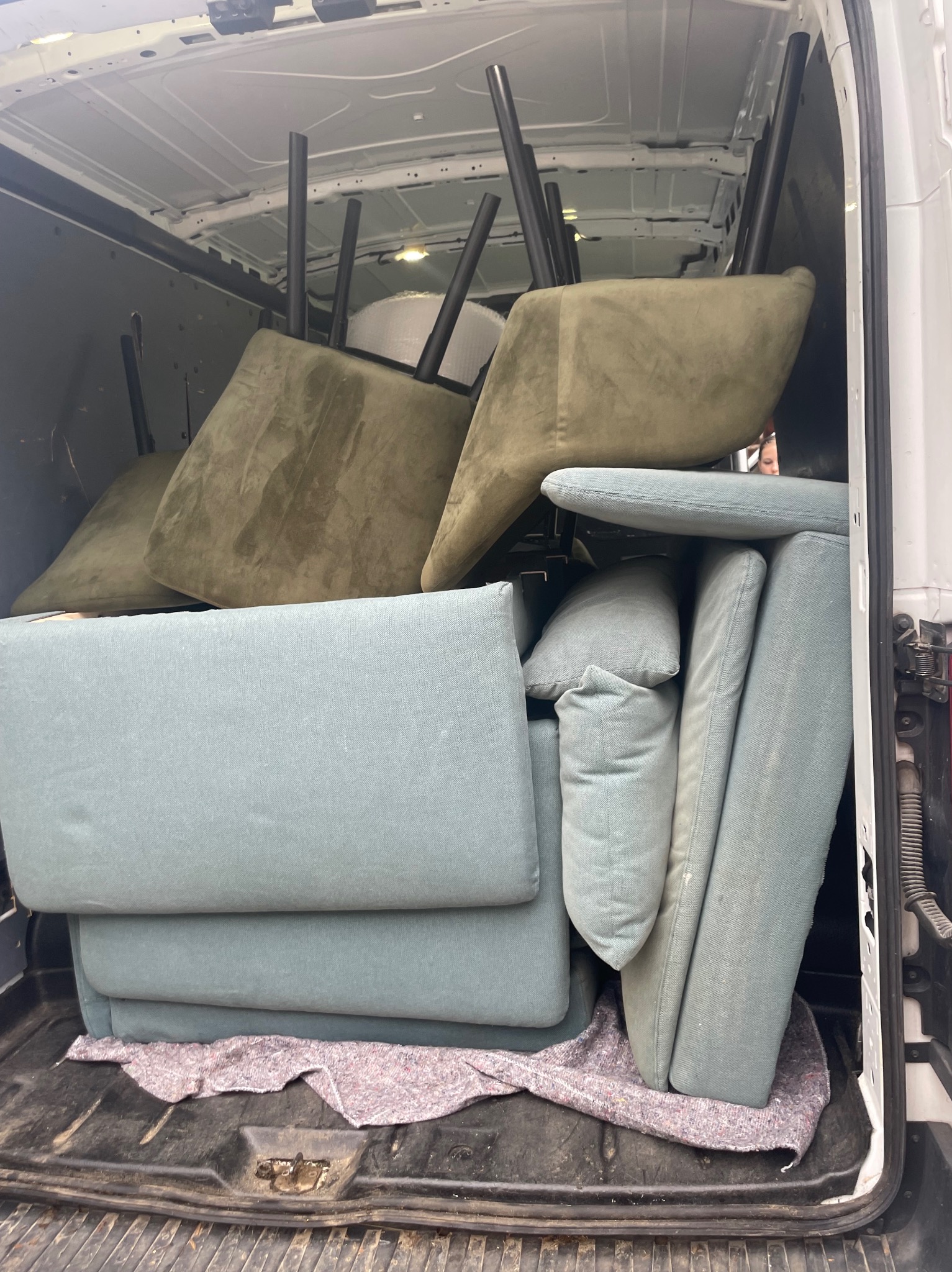 Wnętrze białego busa wypełnione meblami tapicerowanymi w odcieniach zieleni i błękitu, zabezpieczonymi kocem, gotowymi do transportu.