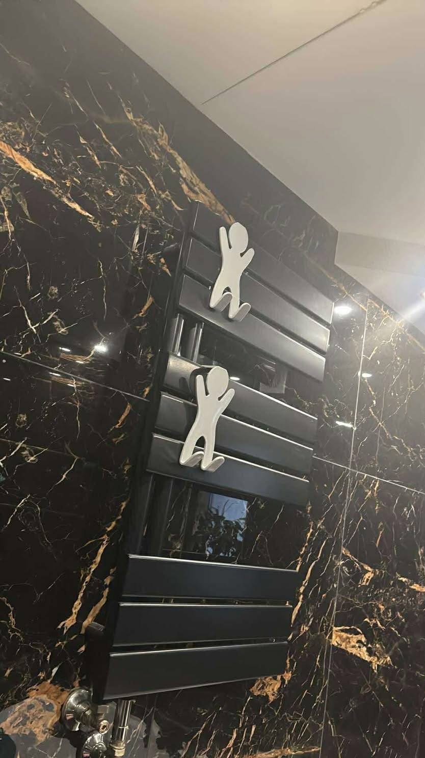 Czarny grzejnik łazienkowy z dekoracyjnymi wieszakami na tle ściany z płytek imitujących czarny marmur ze złotymi żyłami. Nowoczesny design.