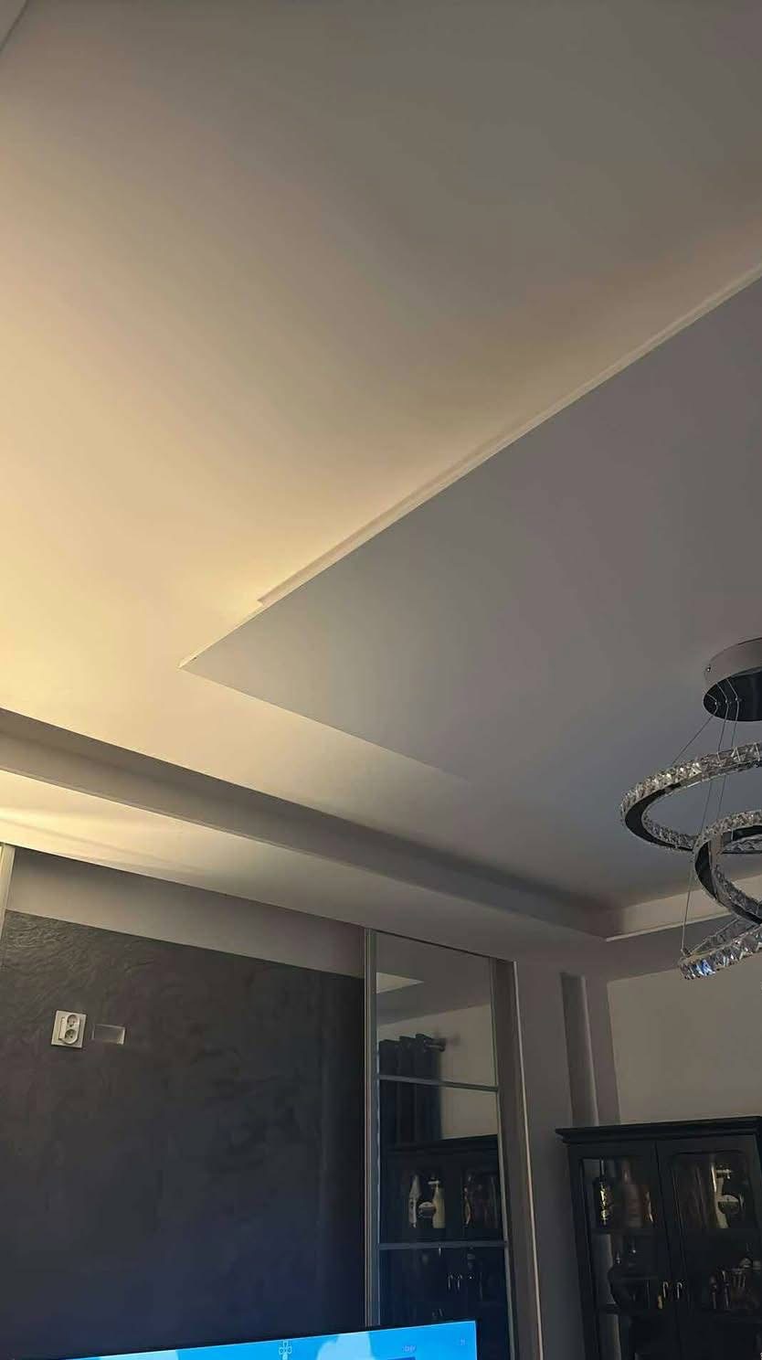 Kaskadowy sufit podwieszany z oświetleniem LED i nowoczesnym żyrandolem. Szara ściana i przesuwne drzwi z lustrami w tle.