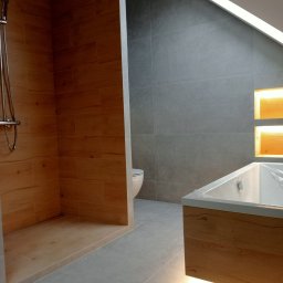 RenovArt - Nowoczesna łazienka na poddaszu: drewnopodobne płytki w strefie prysznica, szare płytki na ścianach, podświetlana wanna. Aranżacja z dbałością o detale.