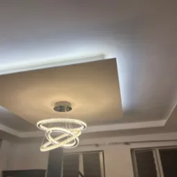 Podwieszany sufit z oświetleniem LED i nowoczesnym żyrandolem. Wykończenie wnętrza z elementami dekoracyjnymi.