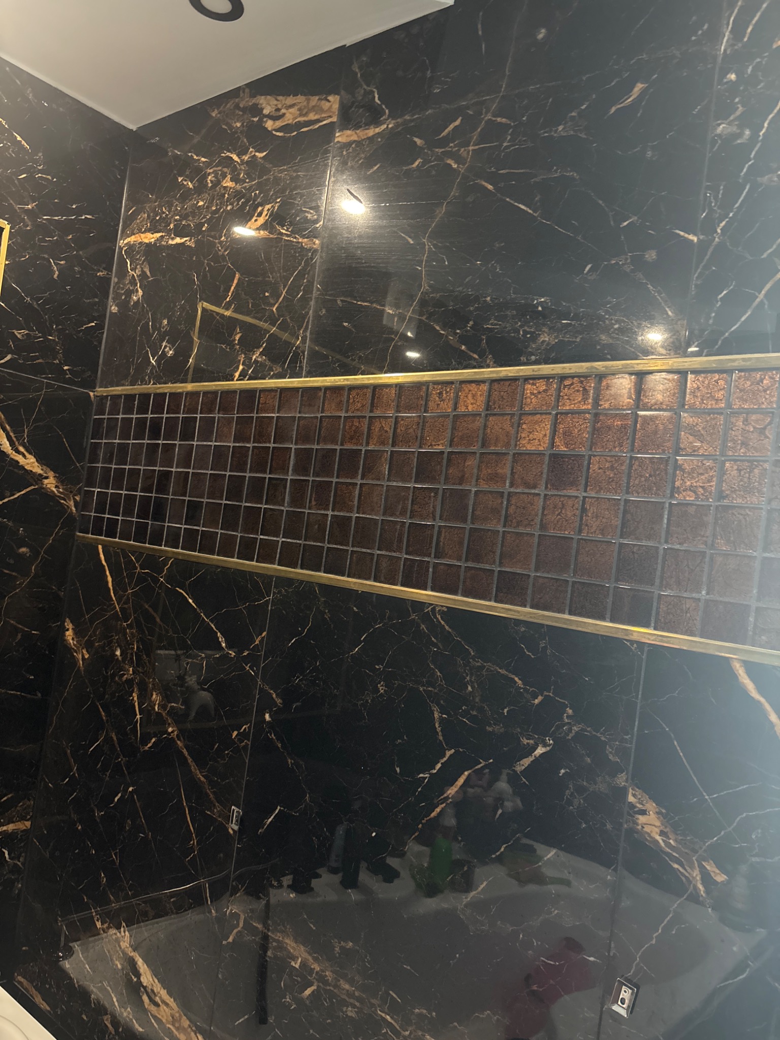 Luksusowa łazienka: czarne marmurowe płytki z złotymi żyłkami i dekoracyjną mozaiką w odcieniach brązu, podkreśloną złotymi listwami.