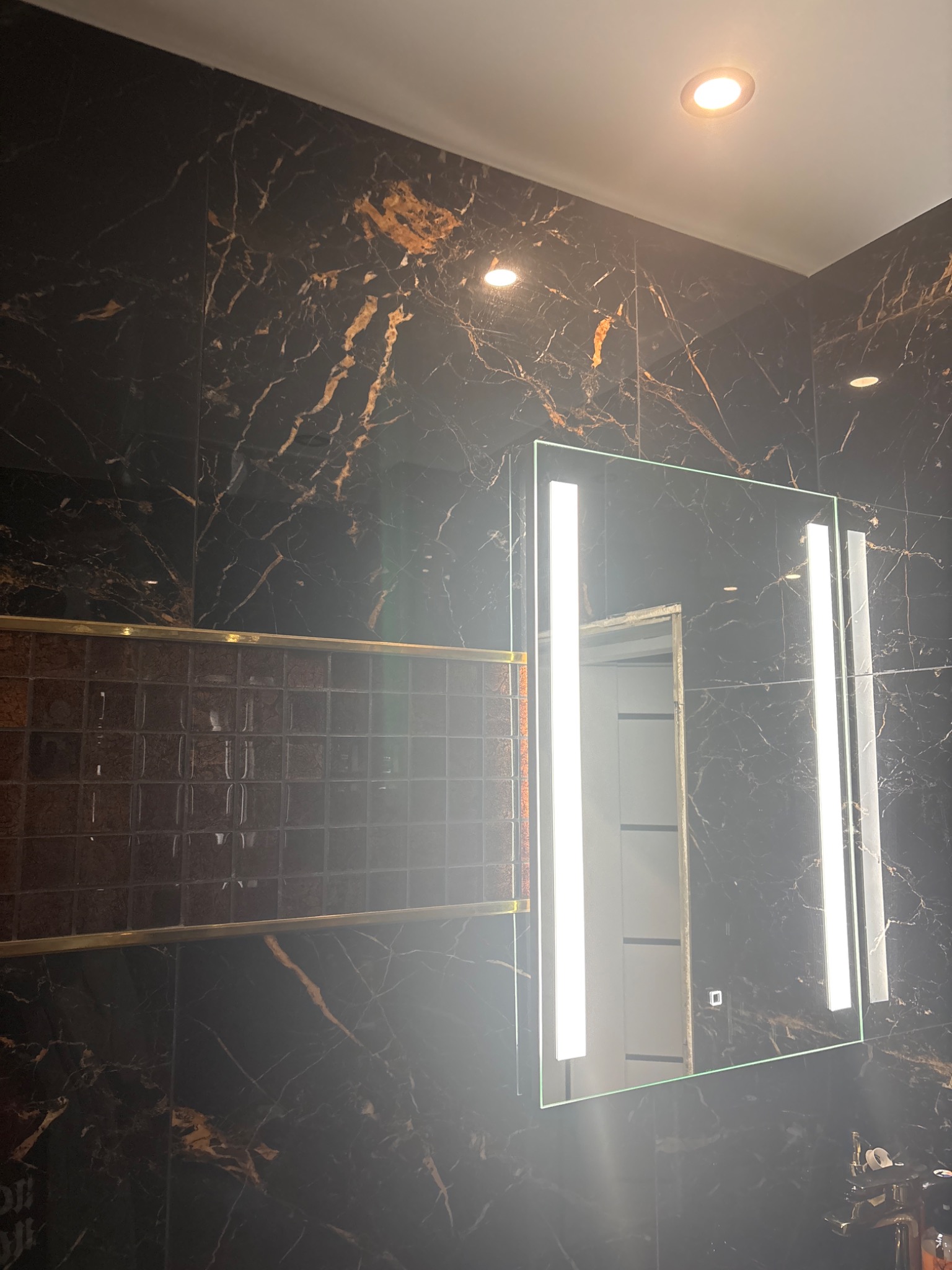 Elegancka łazienka z czarnymi płytkami imitującymi marmur, mozaiką i podświetlanym lustrem. Nowoczesny design z dbałością o detale.