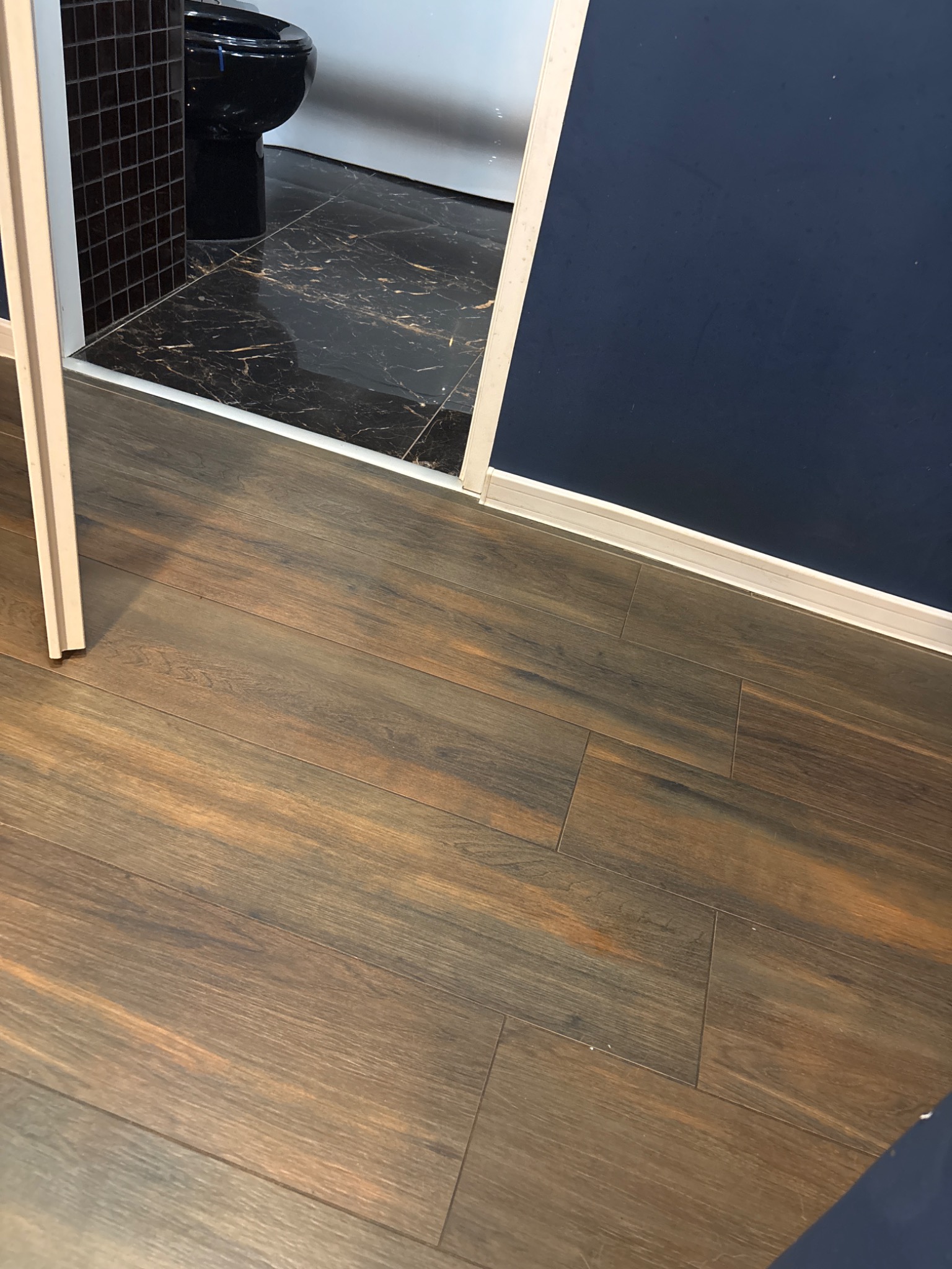 Częściowy widok wykończonej łazienki z drewnopodobną podłogą, czarną toaletą i mozaiką. Kontrastujące kolory i materiały tworzą nowoczesny design.