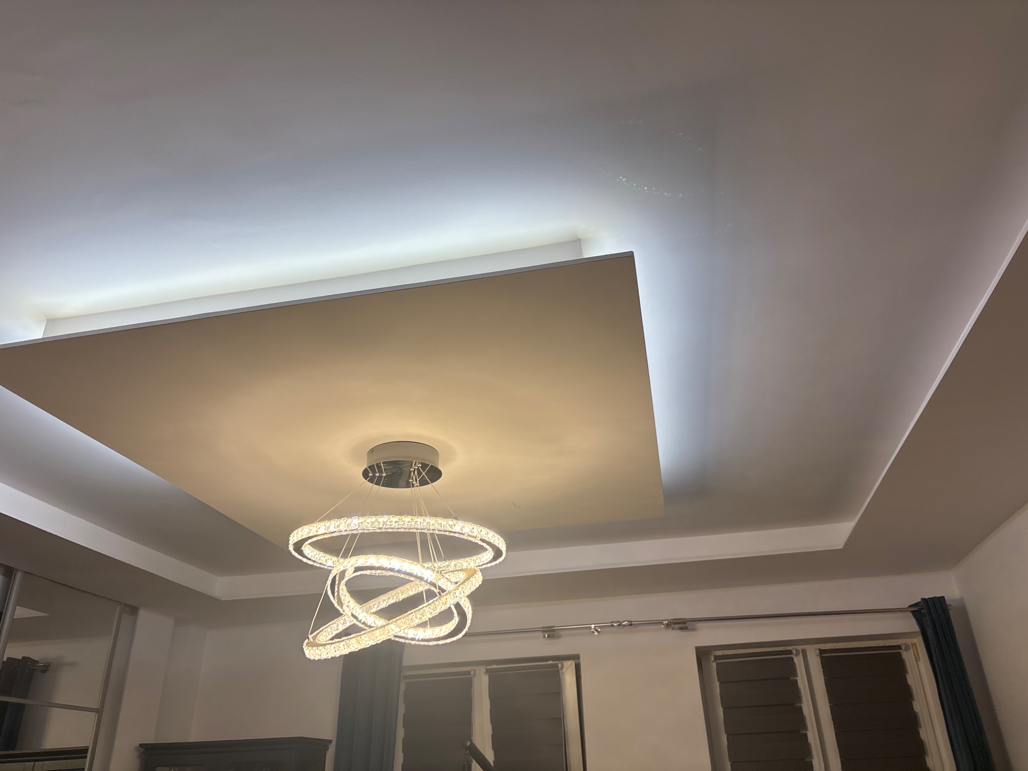 Podwieszany sufit z oświetleniem LED i nowoczesnym żyrandolem. Wykończenie wnętrza z elementami dekoracyjnymi.