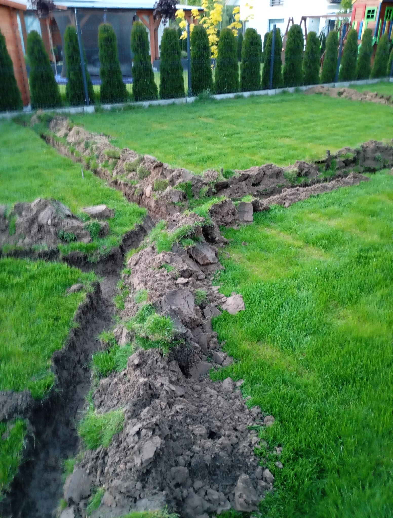 Wykopane rowy w trawie pod system nawadniania ogrodu. Przygotowanie do montażu instalacji nawadniającej. Widoczne świeżo wykopane bruzdy w zielonym trawniku.