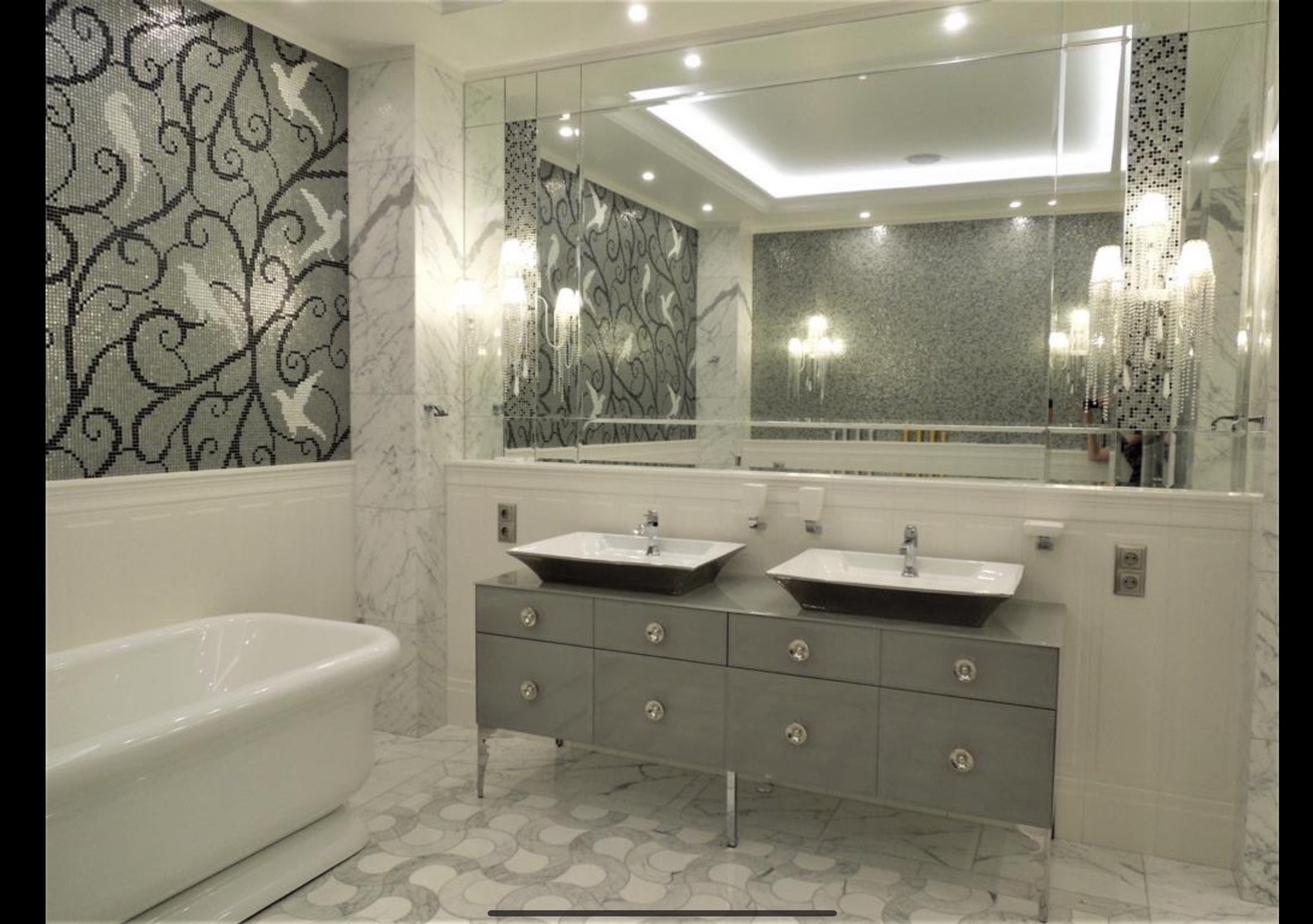 Luksusowa łazienka z mozaiką w ptaki, marmurowymi akcentami i podwójną umywalką na szarej komodzie. Lustro powiększa przestrzeń. Elegancki wystrój.