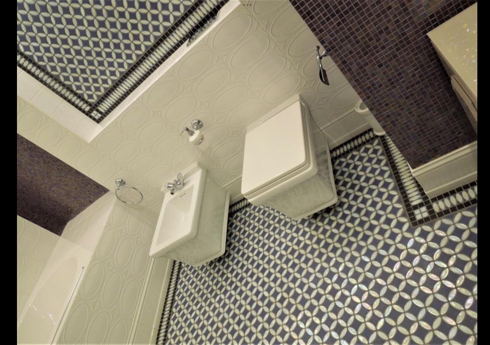 Wykończona łazienka z białą armaturą i mozaiką w odcieniach granatu i bieli na podłodze i suficie. Ściany wyłożone białymi płytkami z tłoczonym wzorem.