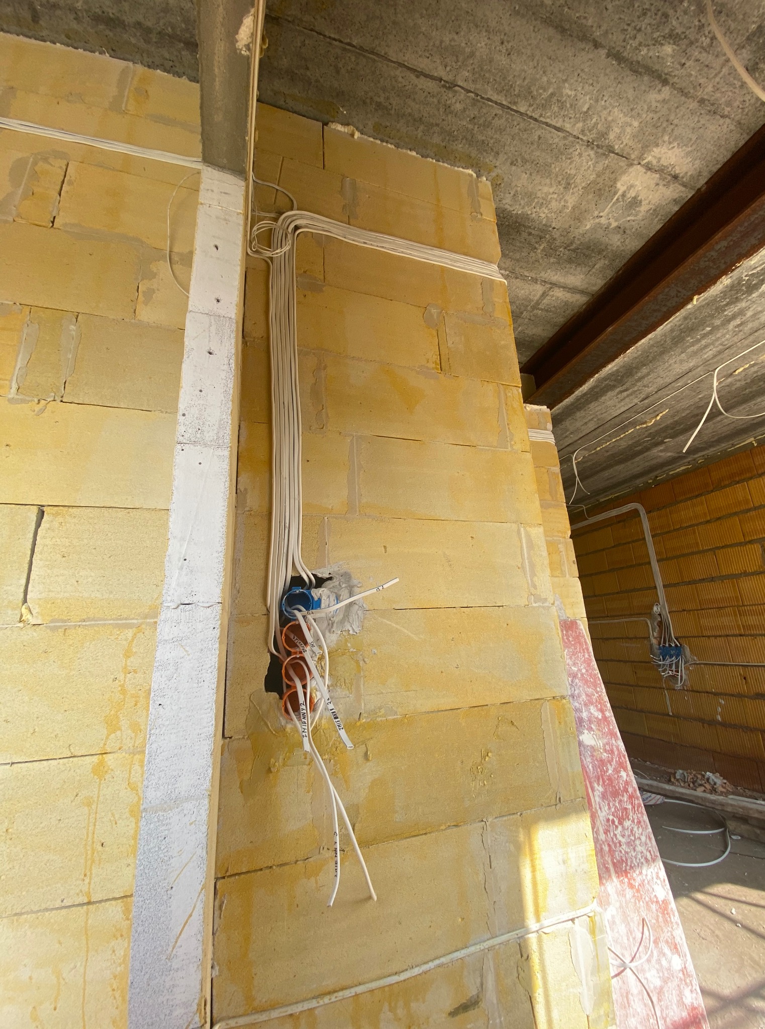 Surowe wnętrze w trakcie budowy: przewody elektryczne w ścianie z bloczków, widoczne puszki instalacyjne i kable ułożone wzdłuż ściany. Betonowy strop z elementami konstrukcyjnymi.