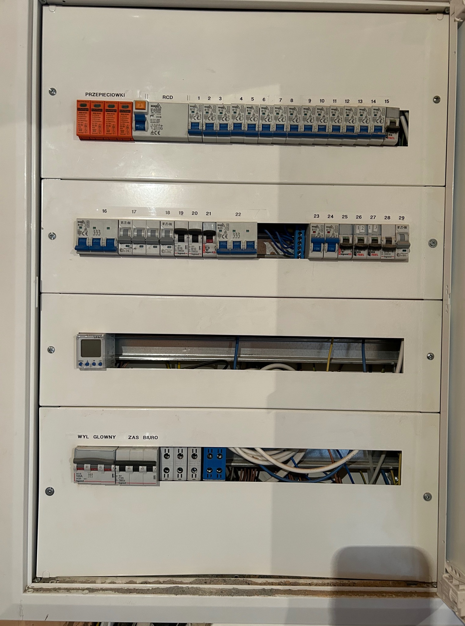 Rozdzielnica elektryczna z bezpiecznikami, wyłącznikami różnicowoprądowymi i ogranicznikiem przepięć. Widoczne okablowanie i oznaczenia.