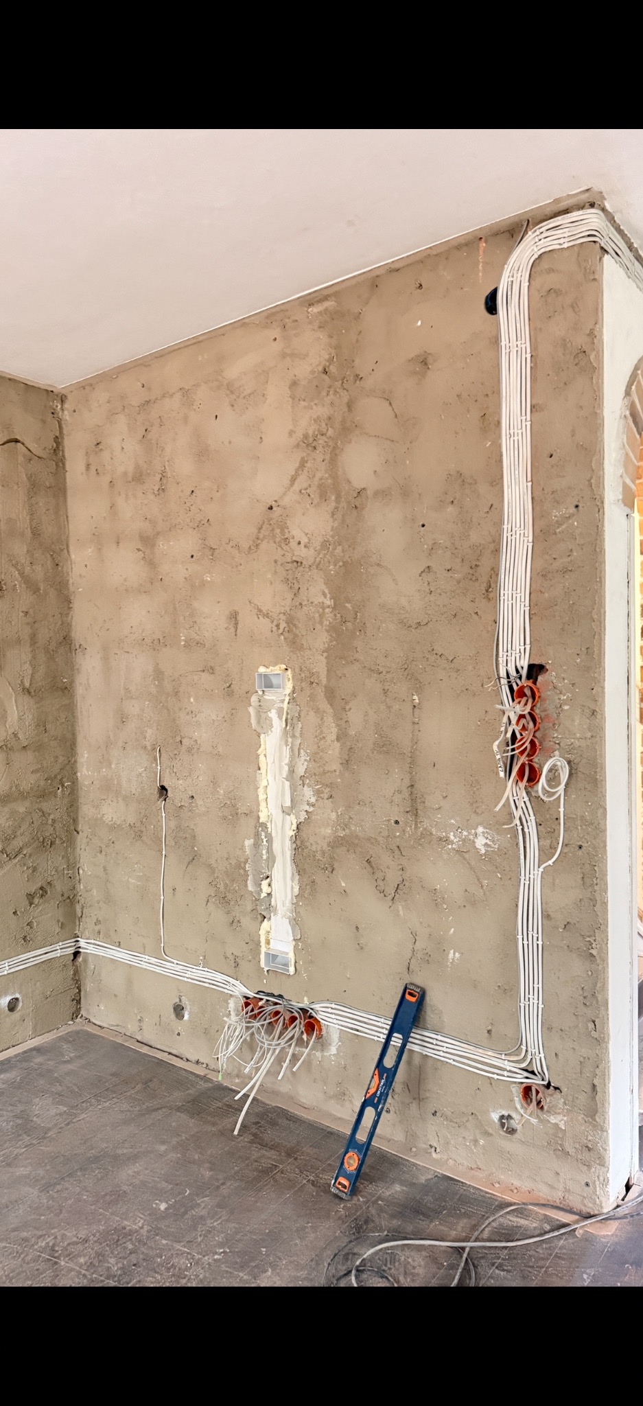 Surowy stan ścian z widoczną instalacją elektryczną w peszlach i puszkach. Poziomica oparta o ścianę. Widok na wnętrze w trakcie prac wykończeniowych.