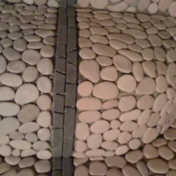 Ściana wykończona jasnymi, owalnymi kamieniami rzecznymi, oddzielona pionowym pasem z ciemnych, prostokątnych płytek.