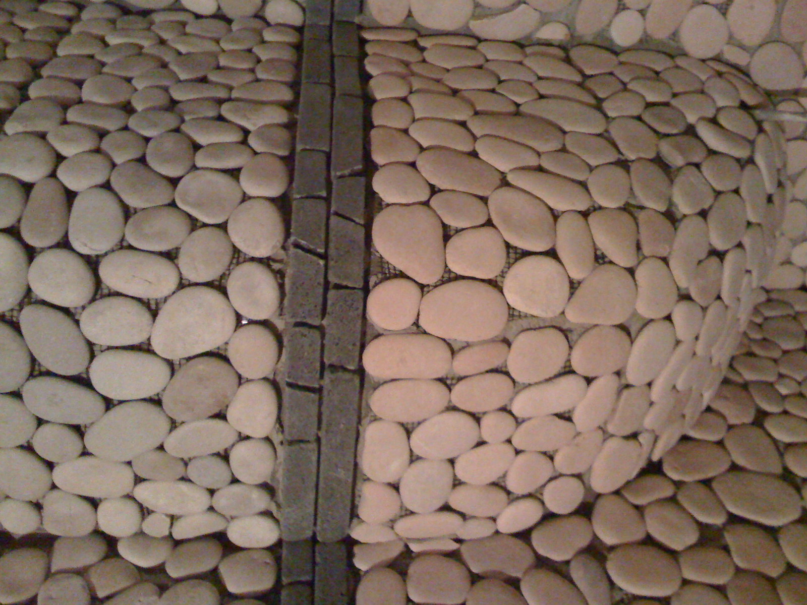 Ściana wykończona jasnymi, owalnymi kamieniami rzecznymi, oddzielona pionowym pasem z ciemnych, prostokątnych płytek.