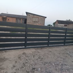 Robstal - Nowoczesna, przesuwna brama wjazdowa w kolorze grafitowym, z poziomymi panelami, na tle wiejskich budynków. Widok z zewnątrz.