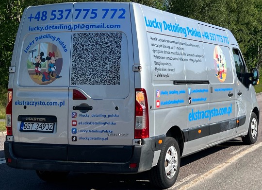 Srebrny van firmy Lucky Detailing Polska z numerem telefonu, adresem e-mail i kodem QR. Na pojeździe grafika z Myszka Miki i Mini oraz lista usług, m.in. mycie okien.