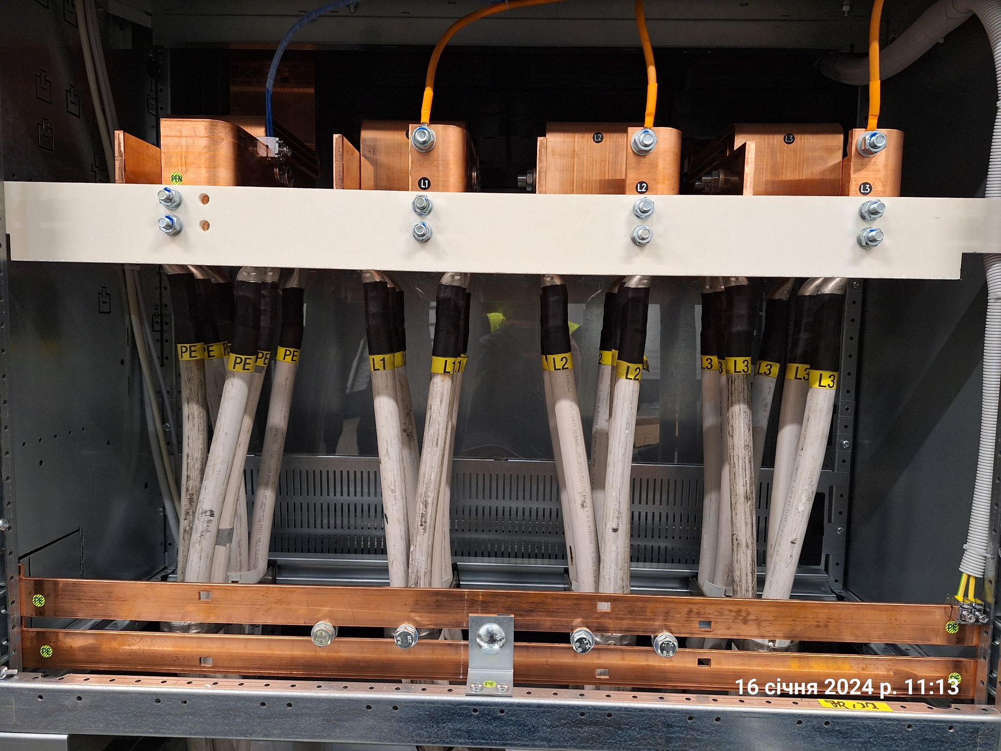 Rozdzielnica elektryczna z miedzianymi szynami, oznaczonymi przewodami PE i L1-L3. Widoczne śruby mocujące i perforowana obudowa. Instalacja wewnątrz szafy sterowniczej.