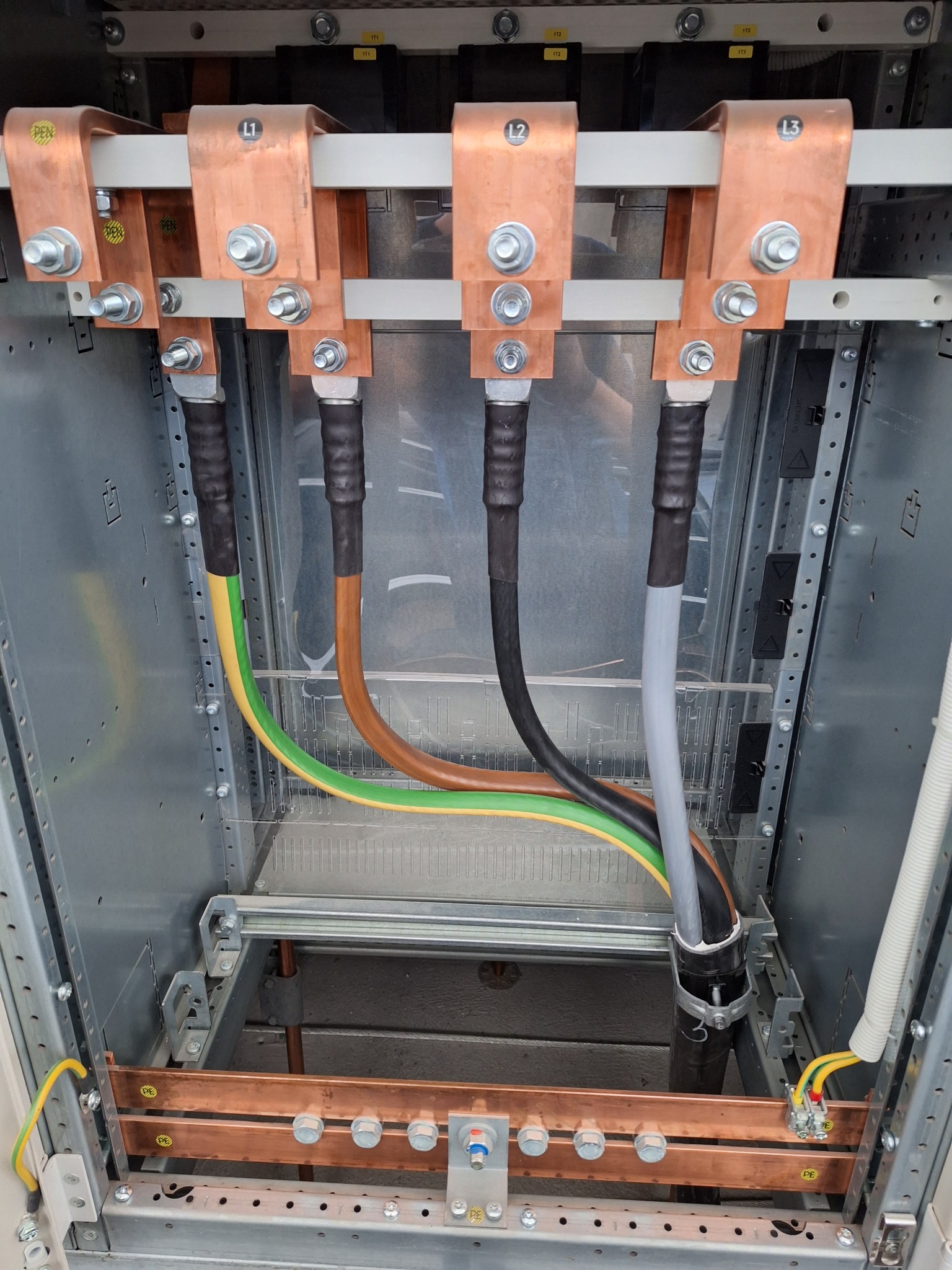 Rozdzielnica elektryczna z miedzianymi szynami oznaczonymi L1, L2, L3 i PEN oraz przewodami w izolacji, widoczne połączenia śrubowe i oznaczenia.