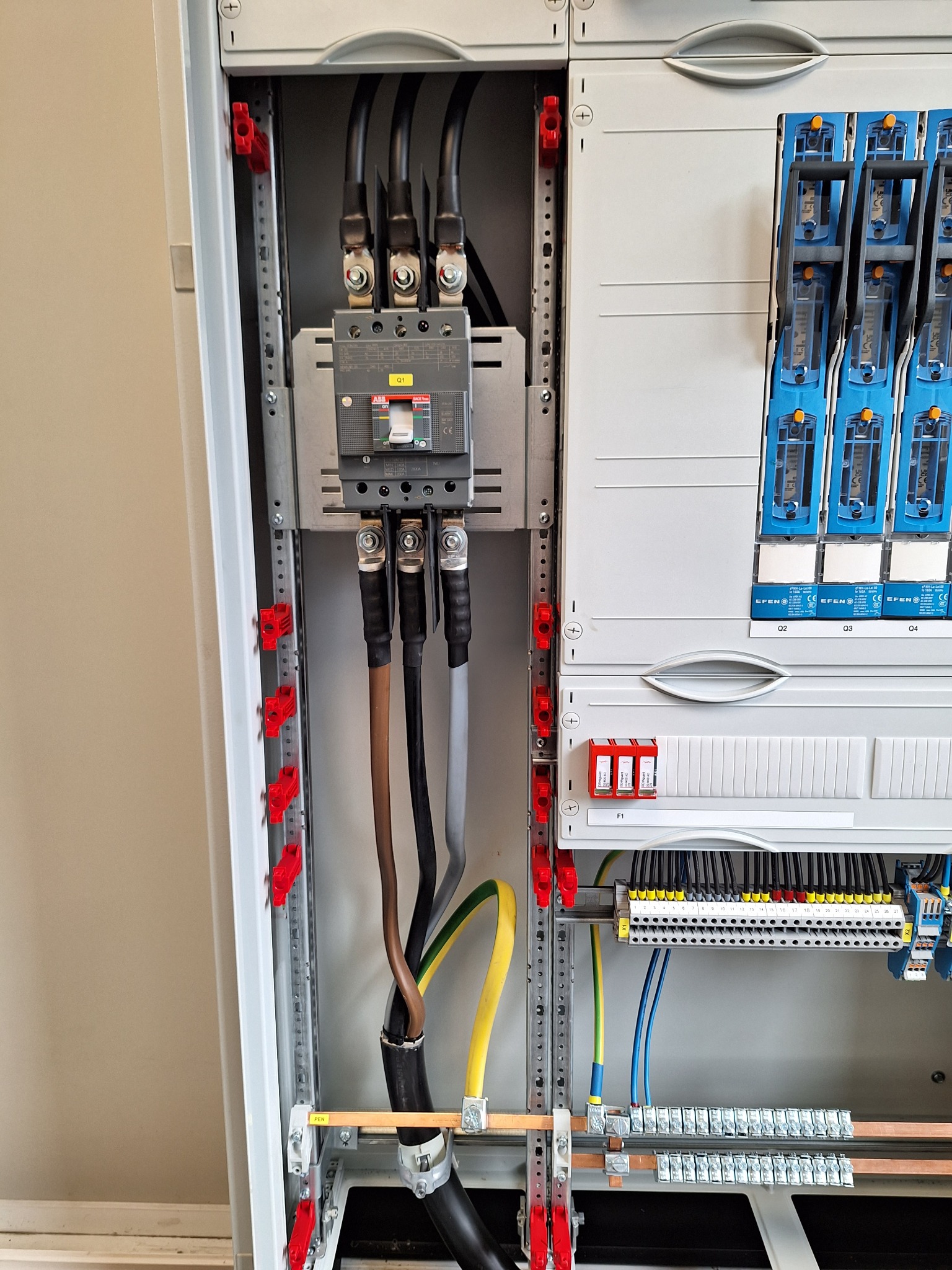 Szczegółowe ujęcie wnętrza rozdzielnicy elektrycznej z widocznymi przewodami, bezpiecznikami i listwami zaciskowymi. Instalacja w szarej obudowie, profesjonalny montaż.